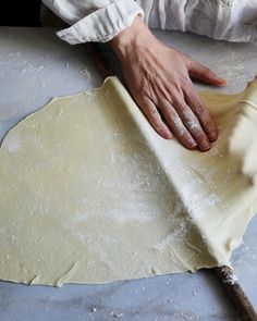 a person kneading dough on top of a table next to a rolling pin
