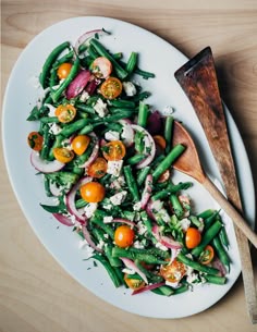 a white plate topped with green beans, onions and oranges next to a wooden spoon