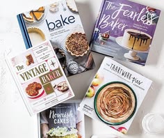 four books are sitting on a white surface next to some glasses and plates with desserts in them