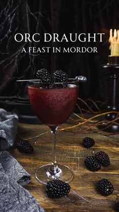 a glass filled with blackberries on top of a wooden table next to some candles