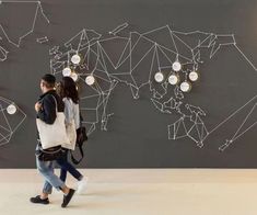 two people walking in front of a wall with a world map on it and lights hanging from the ceiling