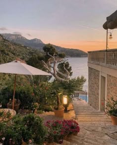an outdoor patio with tables and umbrellas next to the water at sunset or dawn