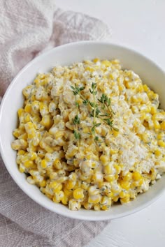 a bowl filled with corn and cheese on top of a white table cloth next to a fork