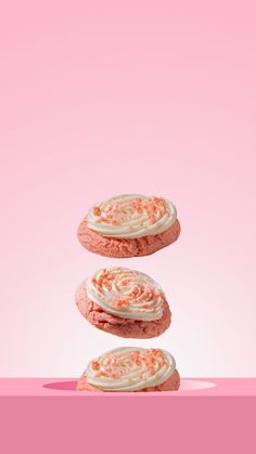 three pink cookies with white frosting and sprinkles are stacked on top of each other