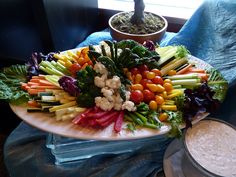 a platter filled with lots of different types of veggies next to a bowl of dip