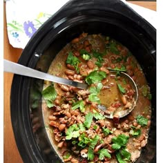 a black crock pot filled with beans and cilantro on top of a wooden table