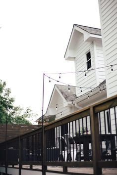 an outdoor patio with string lights on the side of it and a white house in the background