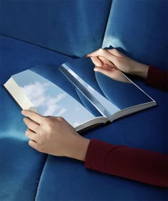 a person is reading a book on a blue couch with their hands resting on the cover