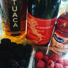 raspberries, blueberries and other fruit are on the table next to wine bottles