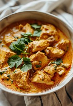 a white bowl filled with chicken curry and garnished with cilantro leaves