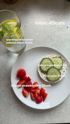 a white plate topped with cucumber and strawberries next to a glass of water