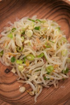 a wooden bowl filled with sprouts on top of a table next to a fork