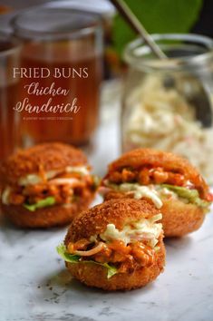 three mini sandwiches sitting on top of a counter next to a jar of macaroni and cheese