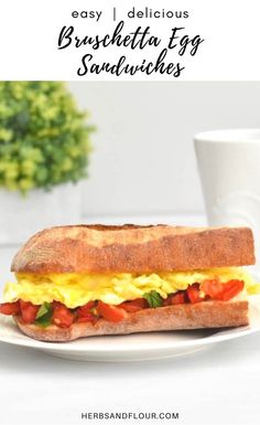 an egg and tomato sandwich on a white plate with a cup of coffee in the background