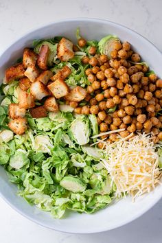 a white bowl filled with lettuce and chickpeas next to shredded cheese