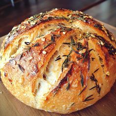 a loaf of bread with rosemary sprigs on top sits on a cutting board