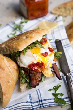 a breakfast sandwich with bacon, eggs and bread on a napkin next to a knife