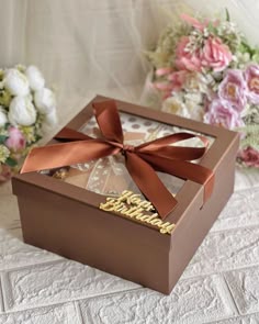 an open box with a ribbon on it sitting on a table next to some flowers