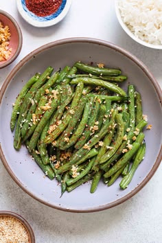 green beans with sesame seeds and seasoning in a bowl next to bowls of rice