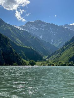 the mountains are covered in snow and green grass, as well as some water with small ripples