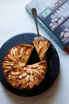 an apple pie on a black plate with a knife and book in the back ground