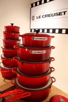 red pots and pans stacked on top of each other in front of a sign that reads le creuset