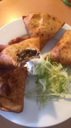a white plate topped with three pieces of food on top of a wooden table next to a green leafy salad