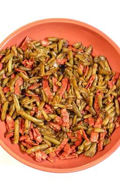 an orange bowl filled with green beans and other food items on a white table top