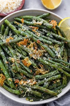 a white bowl filled with green beans covered in parmesan cheese and lemon wedges