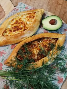 two pieces of pizza sitting on top of a wooden table next to an avocado