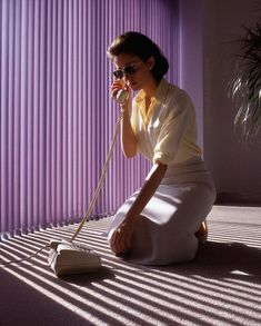 a woman sitting on the floor talking on a phone and holding a cord to her ear