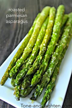 asparagus on a white plate sitting on a wooden table with the words roasted parmesan asparagus