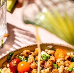 a salad with tomatoes, chickpeas and spinach in a bowl next to a glass of water