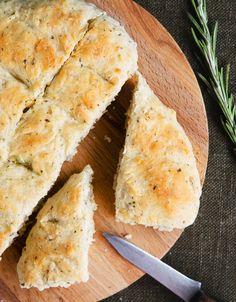 a wooden cutting board topped with pieces of bread next to a knife and sprig of rosemary