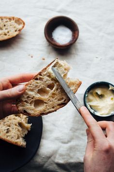 a person holding a knife in their hand over a piece of bread with butter on it