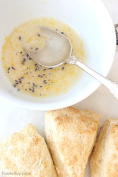a bowl filled with soup next to three scones on a white tablecloth and silver spoon