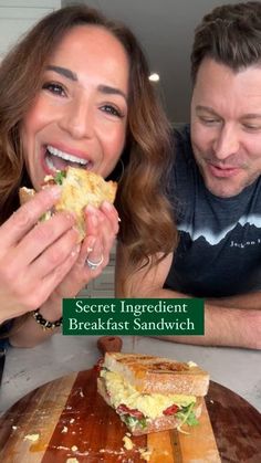 the man and woman are eating sandwiches together at the table in front of them is a sign that says secret ingredient breakfast sandwich