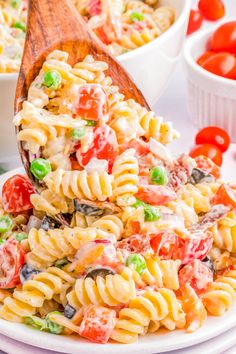 a wooden spoon full of pasta salad on a white plate with tomatoes and green beans