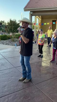 a man standing in front of a building while holding a microphone to his ear and wearing a cowboy hat