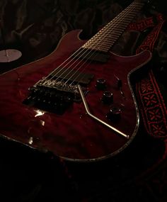 a red electric guitar sitting on top of a black cloth covered floor next to a wine glass