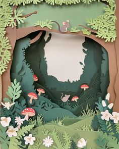 an open cardboard box with paper cut out of trees and mushrooms on the inside, in front of a forest scene