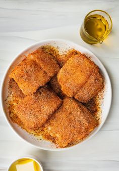 a white plate topped with cut up fish next to two bowls of mustard and seasoning