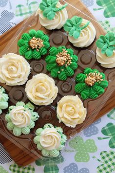 cupcakes decorated with green and white frosting on a wooden platter next to shamrock leaves