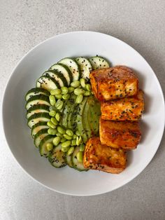 a white plate topped with sliced cucumbers and pieces of meat on top of it