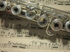 a silver flute with musical notes on it's side and sheet music in the background