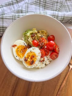a bowl filled with eggs, tomatoes and avocado on top of a wooden table