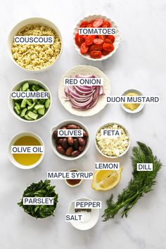 the ingredients to make this salad are displayed on a white counter top, including tomatoes, cucumbers, onions, olives, and other vegetables