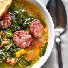 a white bowl filled with sausage and spinach soup next to a piece of bread