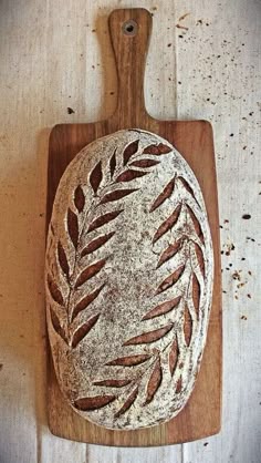 a wooden cutting board topped with a loaf of bread on top of a white table