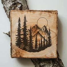 a piece of wood that has some trees on it with mountains in the background and a full moon